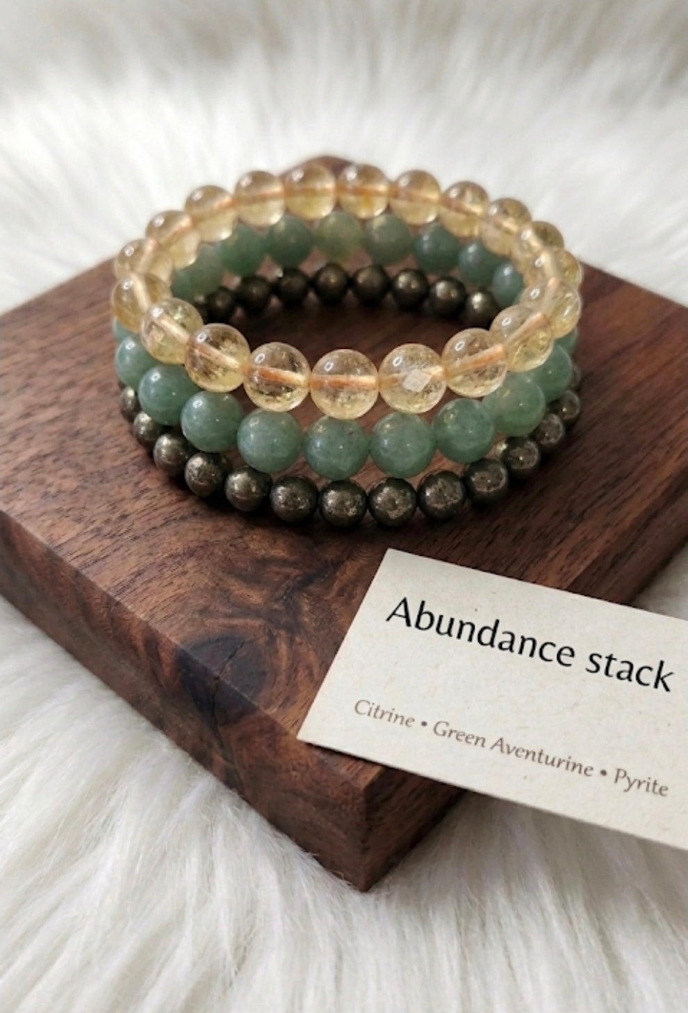 Stack of beaded bracelets on a wooden block with a card labeled 'Abundance stack' on a soft white background.